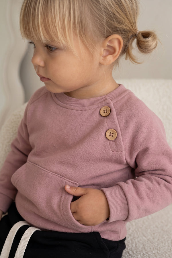 Pudra bebek sweatshirtte ahşap omuz düğmeleri ve ön cep, model üzerinde yakın görünüm | RG401