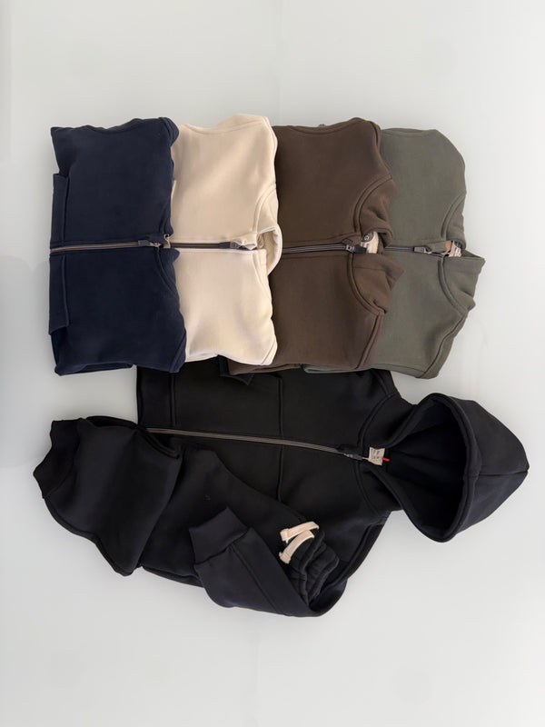 قطع علوية مطوية من طقم RG Brand RG1785 بالكحلي والإكرو والبني والكاكي، بجانب السترة ذات غطاء الرأس والبنطال باللون الأسود.