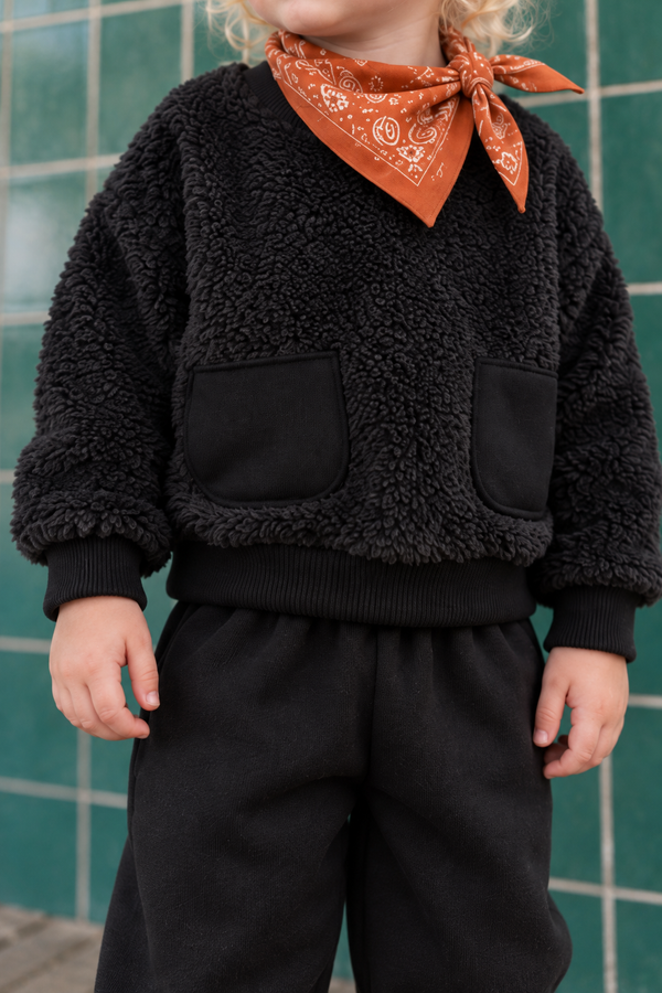 RG356 siyah bebek ikili takımın yakın planı; sweatshirtün peluş dokusu, iki düz kumaş cebi, ribana manşetleri ve eşofman kumaşı.