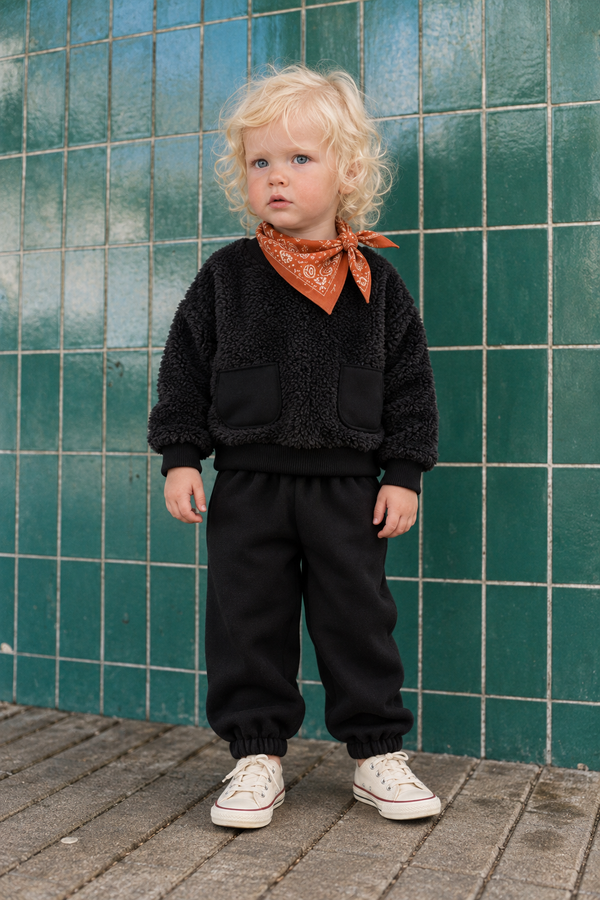 Vorderansicht des schwarzen RG356 Baby-Zweiteilers am Kind: Plüsch-Sweatshirt mit zwei Taschen und Jogginghose mit elastischen Beinabschlüssen.