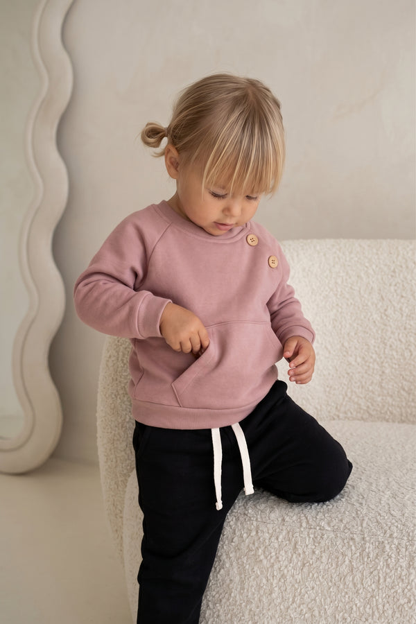 Pudra omuz düğmeli sweatshirt ve siyah eşofman altı giyen oturan kız çocuk | RG401