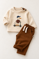 Folded RG Brand RG415 baby outfit with an ecru duck-print top and brown trousers.